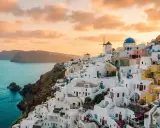 Vacker solnedgång över Oia, Santorini. Vita hus klättrar längs klippan ner mot det turkosblå havet. En dröm om en resa till Grekland.
