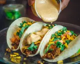 Tre läckra tacos med köttfärs, grönsaker och ost. En krämig sås hälls över dem, perfekt mexikansk mat.