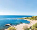 En vacker vy över ett vattenland på Gotland med en sandstrand, klart blått hav och gröna kullar.