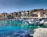 Båtar i en turkos hamn i Calvi, Korsika, med färgglada hus och palmer längs kajen.