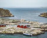 Röda sjöbodar och segelbåtar på klippor vid havet. En idyllisk bild av sommar i Sverige.