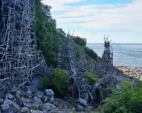 Nimis i Skåne: en skulptur av trä som klättrar uppför klipporna vid havet.