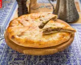 En gyllene, nybakad khachapuri, en klassisk georgisk mat, ligger på en träskärbräda. En bit är uppskuren och visar det smakrika köttfyllningen.
