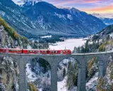 Röda tåget korsar en stenbro över en snöig dal i Schweiz. Fantastiska vyer för din resa till Schweiz tips.