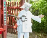 En clown med vit smink och stor hatt håller en nyckel med texten "Dyrehavs Bakken". Han står vid en röd grind.