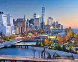 Fakta om New York: En vy över Manhattans skyline vid solnedgången, med den ikoniska One World Trade Center och en modern park vid vattnet.