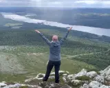 En person med armarna uppsträckta njuter av en fantastisk utsikt över sjöar och skogar under en Lofsdalen vandring.