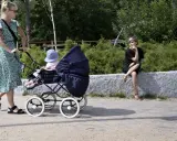 En kvinna med barnvagn njuter av sin semester i Sverige med barn. En annan kvinna sitter på en stenmur i bakgrunden.
