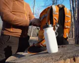 Person packar en orange ryggsäck med vattenflaska. En bra packlista vandring är viktig för äventyret.