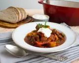 En portion mustig ungersk mat, en mustig gryta med kött och grönsaker, toppad med gräddfil och persilja. Serveras med gott bröd.