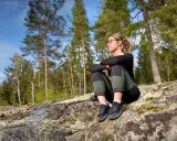 En kvinna vilar på en klippa under en vandring. Solen skiner genom träden, perfekt för vandring rundslingor Stockholm.