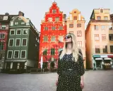En kvinna med solglasögon står framför färgglada hus på ett torg. Kanske är detta sveriges vackraste stad?