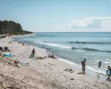 Människor njuter av solen och havet på sveriges finaste strand. Barn leker i vattnet medan andra kopplar av på sanden.
