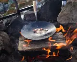 Stekt fläsk i stekpanna över öppen eld, en del av ett recept kolbullar. Elden sprakar och röken stiger.