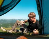 Man gör kaffe vid tältöppningen under en vandring i Sverige sommar. Vacker utsikt över fjällen.