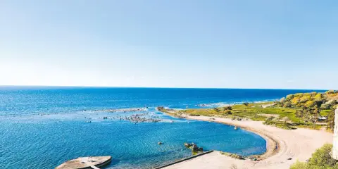 En vacker vy över ett vattenland på Gotland med en sandstrand, klart blått hav och gröna kullar.