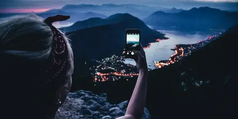 En person tar bild med mobiltelefonen av en stad vid havet i skymningen. En perfekt vy under en bilsemester Europa.