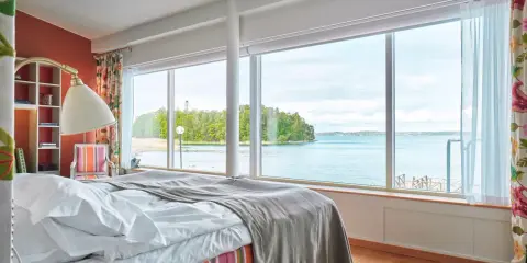Sovrum med fantastisk havsutsikt, perfekt för ett bra hotell i Stockholm. Säng med vita lakan och grå pläd, färgglad randig sängkjol.