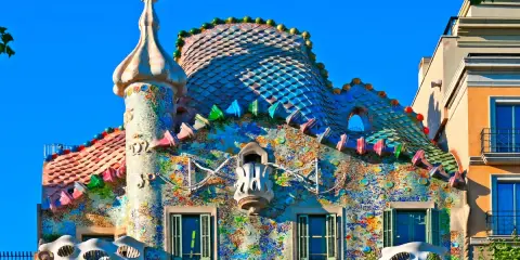 Färgglatt och fantasifullt **Gaudi hus Barcelona** med mosaiktak och unika balkonger under en klarblå himmel.