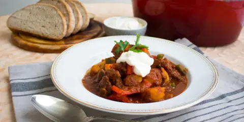 En portion mustig ungersk mat, en mustig gryta med kött och grönsaker, toppad med gräddfil och persilja. Serveras med gott bröd.
