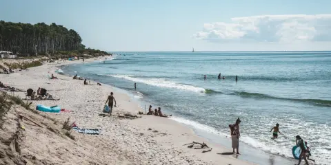 Människor njuter av solen och havet på sveriges finaste strand. Barn leker i vattnet medan andra kopplar av på sanden.
