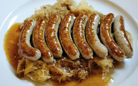 En tallrik med flera saftiga, gyllene tysk korv serverad på surkål med en smakrik sås.
