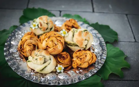 En silverbricka fylld med vackert formade vegetariska pizzabullar, dekorerade med små vita blommor och gröna blad.
