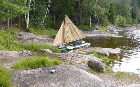 En liten segelbåt med åror ligger vid en stenig strand. En härlig plats att paddla Dalslands kanal på.