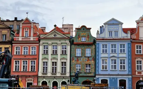 Färgglada husfasader i **Poznan, Polen**, med detaljerade ornament och tak. En byggkran syns i förgrunden.