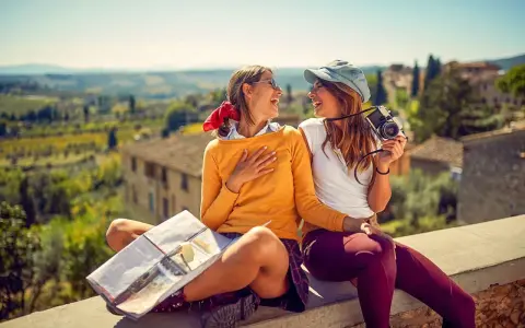 Två glada vänner njuter av sin resa i Europa, med en karta och kamera redo för nya äventyr i en vacker italiensk landskapsvy.