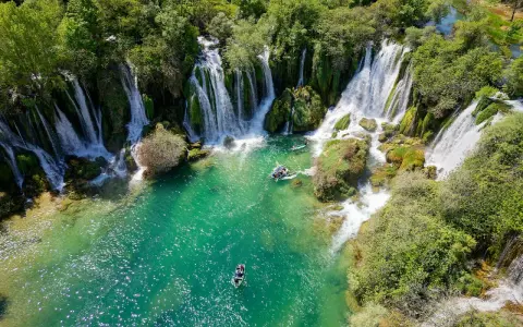 Vackra Kravice vattenfall med turkost vatten och båtar som glider fram. En idyllisk plats för avkoppling.