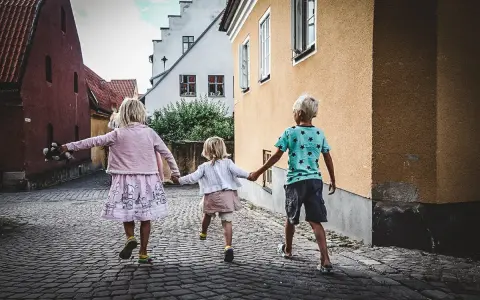 Tre barn håller varandra i handen på en kullerstensgata på Gotland, på väg mot äventyr.