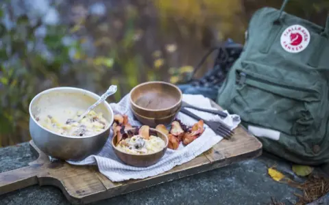 En härlig måltid med pasta och svamp, perfekt för att torka kyckling och njuta av naturen. En Fjällräven ryggsäck och vandringskängor syns i bakgrunden.