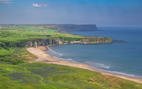 Grönskande kullar och en sandstrand vid havet på Irland, nära Belfast.
