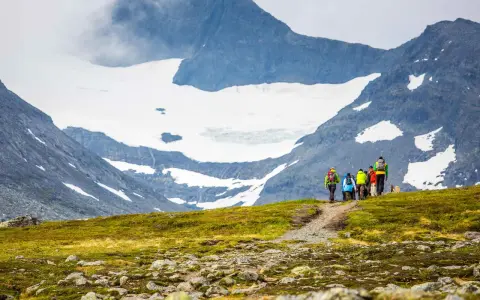 Vandringsgrupp på väg uppför en stenbelagd stig mot Sylarnas glaciärklädda toppar.