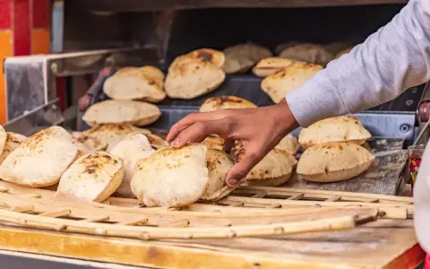 En hand tar färskt, fluffigt bröd från en ugn. Detta är en del av den autentiska egyptiska maten, perfekt för att doppa i läckra röror.