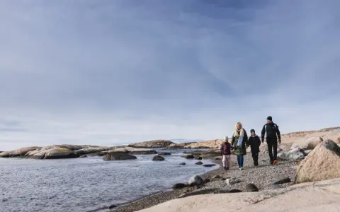 Familj promenerar längs en stenig strand vid Tjurpannans naturreservat.