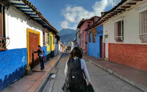 Färgglada hus i La Candelaria, Bogotá. En kvinna med ryggsäck går längs en kullerstensgata. Här finns fakta om Colombia.