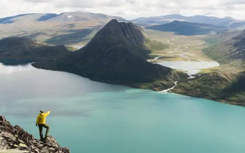Vandrare pekar ut över turkost vatten och berg under en Besseggen vandring.