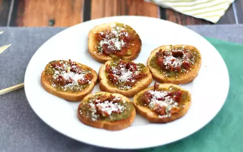 Små, rostade brödskivor toppade med grönt pesto, soltorkade tomater och riven ost. Perfekt som en enkel pesto toast.