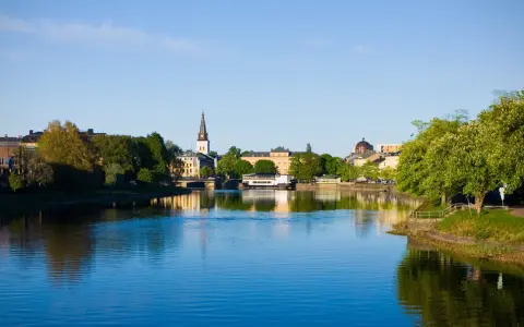 Vacker vy över Klarälven med stadens silhuett, kyrktorn och grönska. En perfekt plats att se i Karlstad en solig dag.