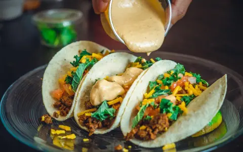 Tre läckra tacos med köttfärs, grönsaker och ost. En krämig sås hälls över dem, perfekt mexikansk mat.