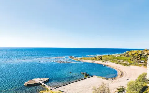 En vacker vy över ett vattenland på Gotland med en sandstrand, klart blått hav och gröna kullar.
