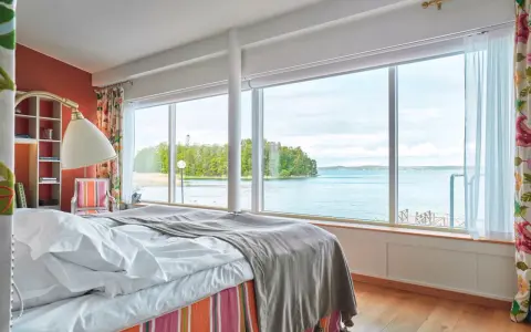 Sovrum med fantastisk havsutsikt, perfekt för ett bra hotell i Stockholm. Säng med vita lakan och grå pläd, färgglad randig sängkjol.
