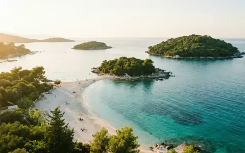 Vacker strand med turkost vatten och gröna öar. Perfekt för en resa till Albanien med tips om sol och bad.