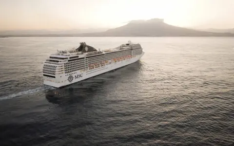 Kryssningsfartyget MSC Poesia glider fram på havet i solnedgången, med en vulkan i bakgrunden.