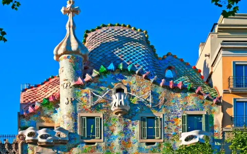 Färgglatt och fantasifullt **Gaudi hus Barcelona** med mosaiktak och unika balkonger under en klarblå himmel.
