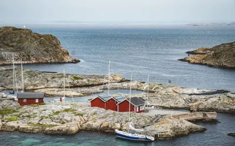 Röda sjöbodar och segelbåtar på klippor vid havet. En idyllisk bild av sommar i Sverige.