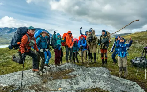 Glada vandrare, redo för Fjällräven Classic i svenska fjällen. De hoppar av glädje på en sten.
