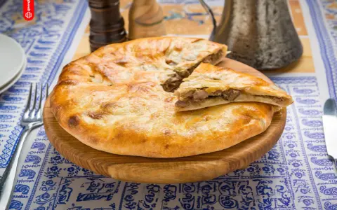 En gyllene, nybakad khachapuri, en klassisk georgisk mat, ligger på en träskärbräda. En bit är uppskuren och visar det smakrika köttfyllningen.